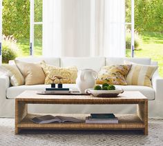 a living room with white couches and pillows on the coffee table in front of large windows