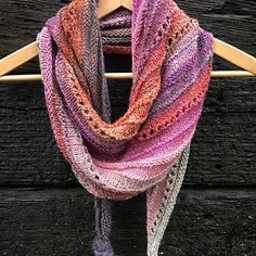 a multicolored knitted scarf hanging on a wooden hanger with clothes pins