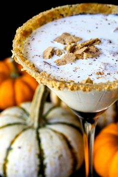 a drink in a martini glass with pumpkins around it