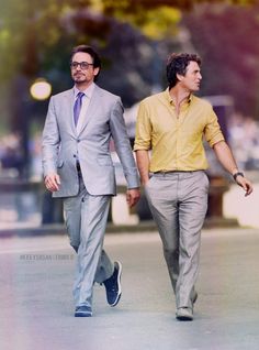 two men in suits are walking down the street, one is wearing a yellow shirt