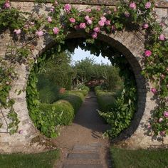 a stone archway with pink roses growing on it's sides and an opening to the garden