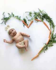 a baby laying on its back in front of carrots and parsley with the shape of a heart