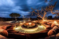 an outdoor fire pit surrounded by couches and lights