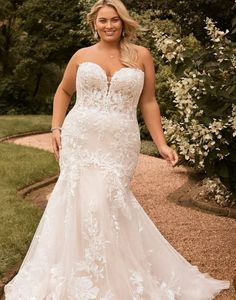 a woman in a white wedding dress standing on a path with trees and bushes behind her