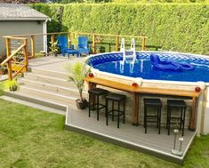 an above ground swimming pool surrounded by grass and wooden decking with bar stools