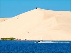 people are riding water skis in the ocean near sand dunes and blue sky with white clouds