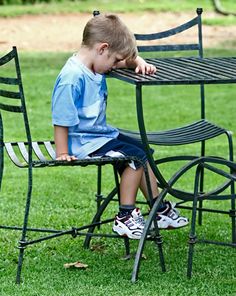 a little boy sitting on top of a metal chair next to a table and chairs