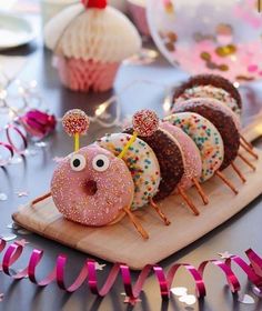 donuts with sprinkles and eyes are on a wooden board next to pink streamers
