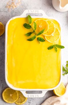 a white dish filled with lemon curd next to sliced lemons and mint leaves