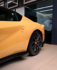 a yellow sports car parked in front of a glass building with an electric charger plugged into it