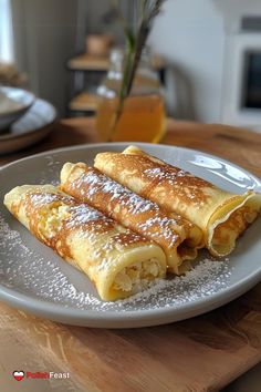 two crepes on a plate with powdered sugar and orange juice in the background