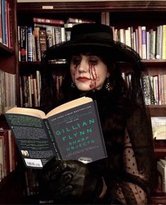 a woman sitting in front of a bookshelf holding an open book with blood on her face