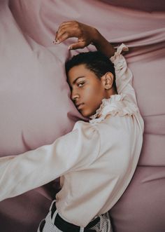 a woman laying on top of a pink bed covered in sheets and pillows with her hand resting on the pillow
