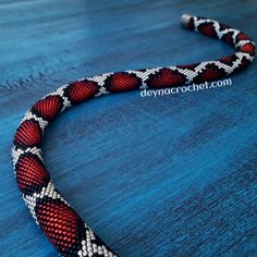 a red, white and black beaded necklace on a blue surface with the words deyacrochet com written below it