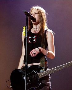 a woman holding a guitar and singing into a microphone