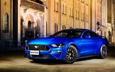 a blue ford mustang parked in front of a large building at night with its lights on