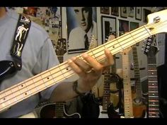 a man playing an electric bass guitar in front of a wall with pictures on it