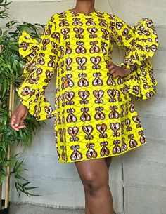 a woman standing in front of a plant wearing a yellow dress with monkeys on it