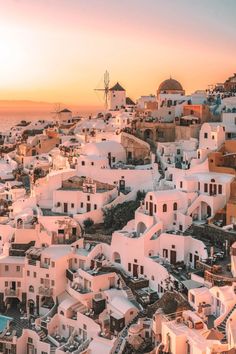 the sun is setting over some white buildings in oia, with windmills on top
