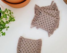 two crocheted potholders sitting on top of a table next to a plant