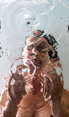 a person's reflection in the water with their hand under them and his face obscured by the water