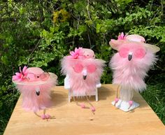 three little pink birds wearing hats on top of a wooden table