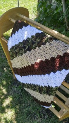 a crocheted blanket sitting on top of a wooden rocking chair in the grass