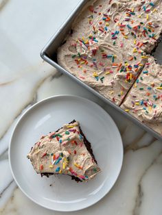 a piece of cake sitting on top of a white plate next to a pan filled with frosting and sprinkles