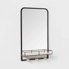 a mirror and shelf on the wall in front of a white wall with a black frame