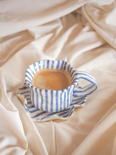 a coffee cup sitting on top of a bed covered in white and blue striped sheets
