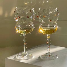 two wine glasses sitting next to each other on a white counter top with lights in them