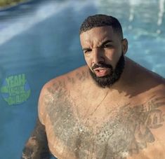 a man with tattoos on his chest standing next to a swimming pool and looking at the camera