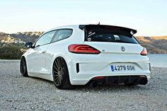 the rear end of a white car parked on gravel