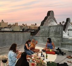 four women sitting on the roof eating and drinking while one woman sits next to her