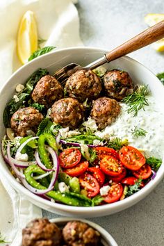 a bowl filled with meatballs and veggies on top of a white table
