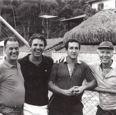 black and white photograph of four men posing for the camera in front of a fence