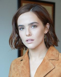 a woman with short hair wearing a tan jacket and gold hoop earrings on her left ear