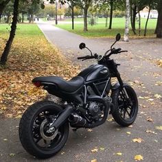 a black motorcycle parked on the side of a road in front of trees and leaves
