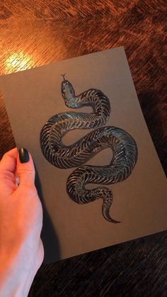 a hand holding a piece of paper with a drawing of a snake on it