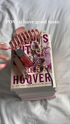 a book with pink nail polish on top of it next to a person's hand