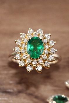 an emerald and diamond ring on a wooden table with other jewelry items in the background