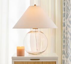 a table with a lamp on top of it next to a dresser and window curtain