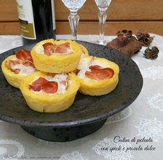 three small pastries on a black plate with white tablecloth and wine bottles in the background