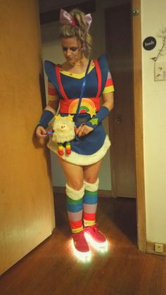 a woman dressed up as a clown holding a stuffed animal in her hand and standing next to a door