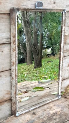 a mirror sitting on the side of a wooden wall next to a tree and grass