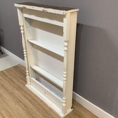 an old white bookcase is sitting on the floor in front of a gray wall