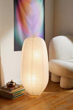 a white lamp sitting on top of a wooden floor next to a chair and books