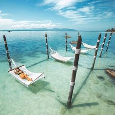 a woman laying in a hammock between two poles on the water with an island in the background