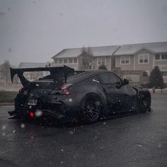 a black sports car parked in front of a house on a rainy day with its hood open