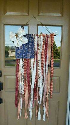 an american flag hanging from the front door with ribbons attached to it and flowers on top